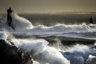 Heavy seas breaking against rocks and the Raz the Sein lighthouse